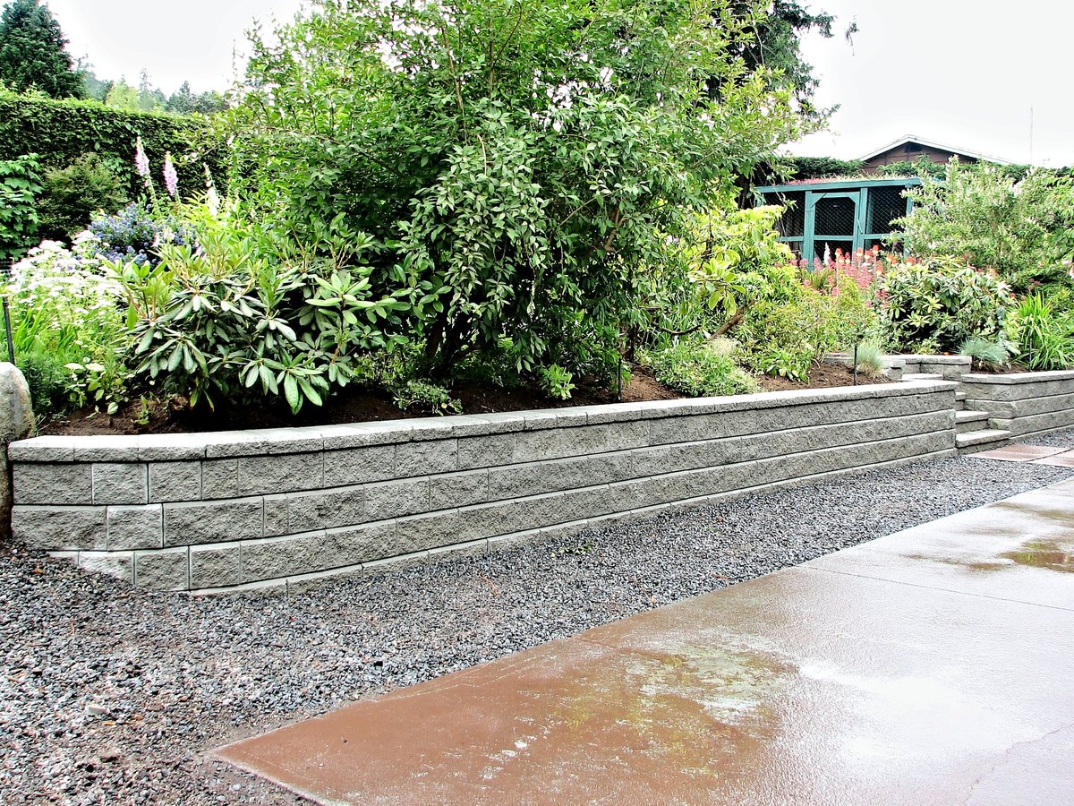 A gray block retaining wall built into an existing garden landscape