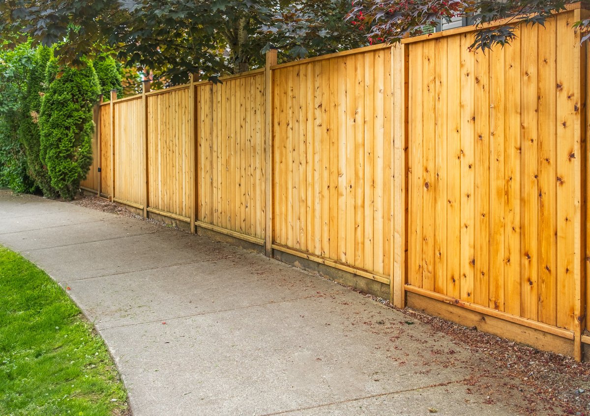 A new cedar wood privacy fence surrounding a home with green lawn and trees