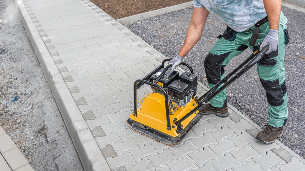 A worker compacting paver blocks into place with a vibrating compaction plate