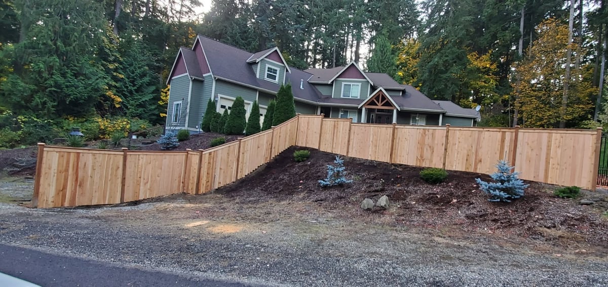 Two-story house with wooden fence and mulched yard in forested residential area