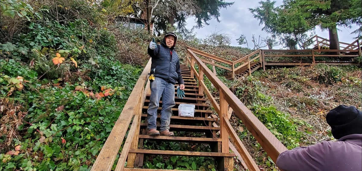 Person climbing wooden stairs on a hillside surrounded by green vegetation and trees